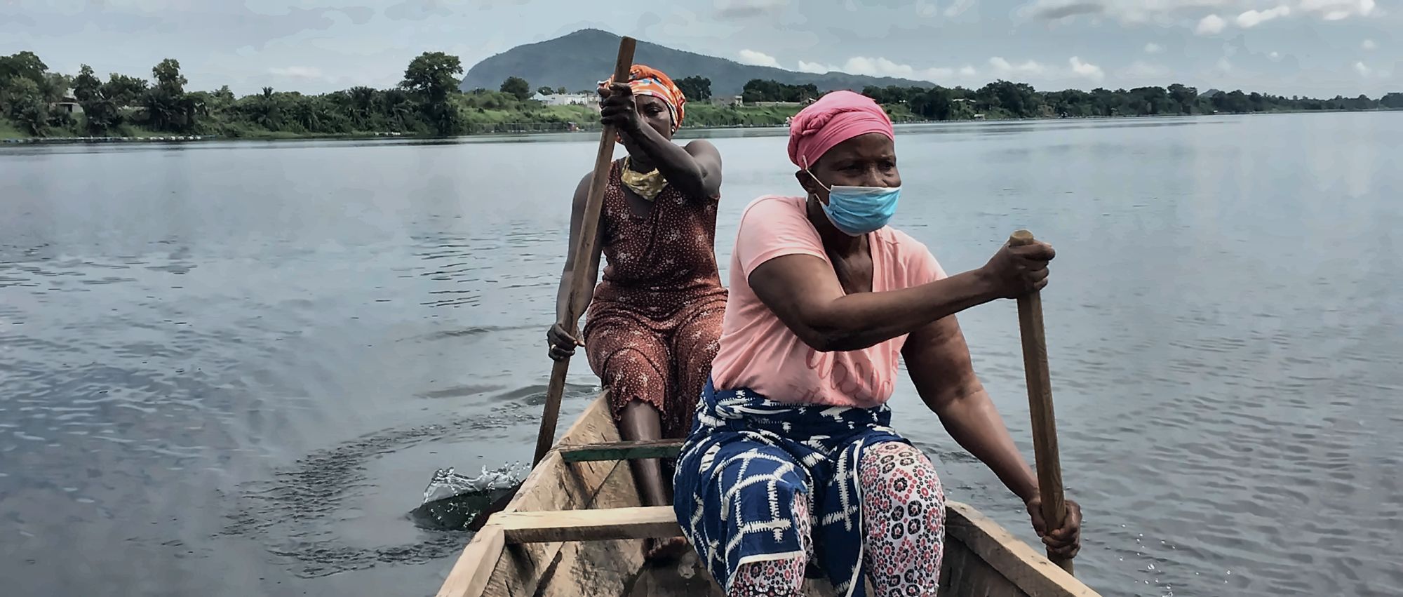 Two women paddling a dugout canoe across open water